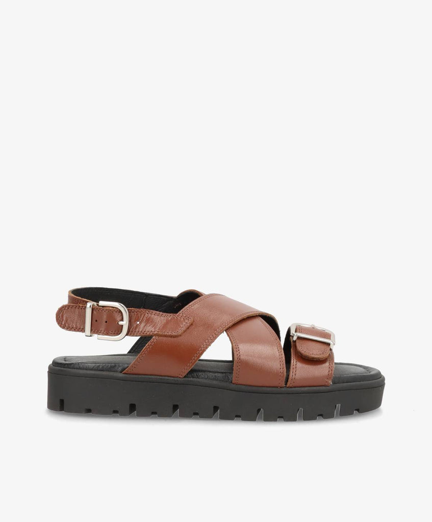 Mørkebrune skindsandaler fra Shoedesign Copenhagen med sort bund og krydsremme. Sandalerne har derudover justerbar ankelrem.