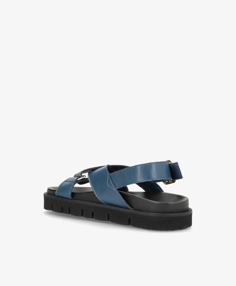 Blå damesandal med krydsede stropper og sort sål, set fra siden.