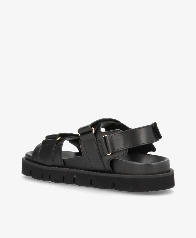 Sort damesandal med justerbare stropper og flad sål.