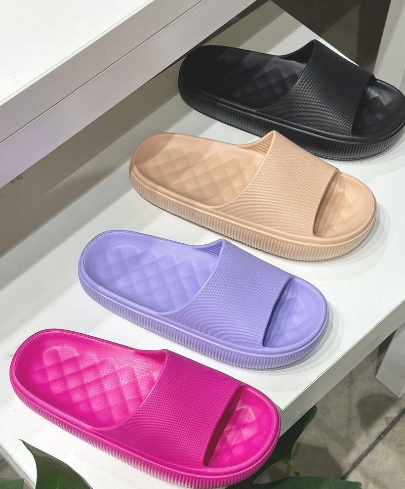 Fire par hjemmesko i forskellige farver: sort, beige, lilla og pink, placeret på en hvid overflade.